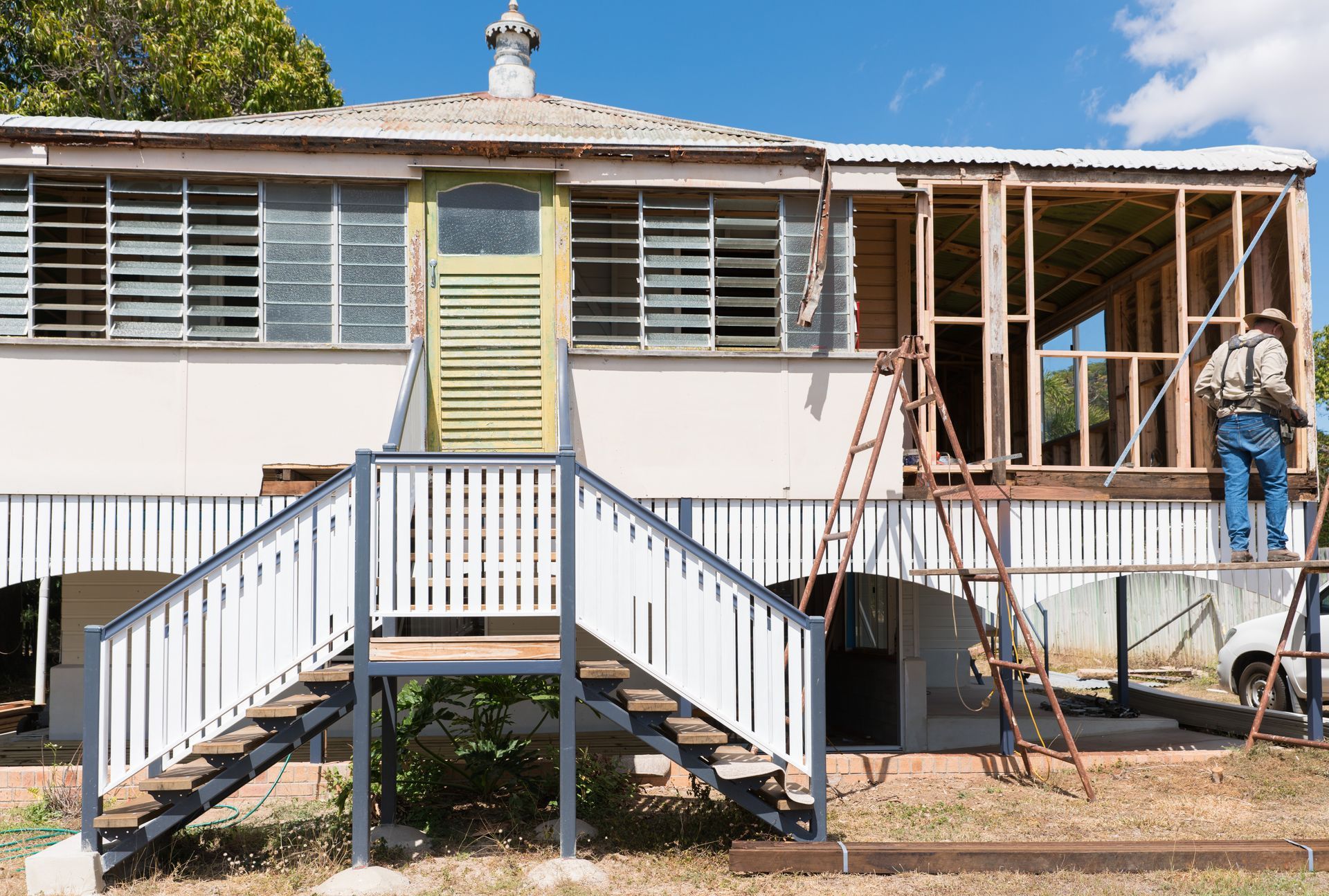 A man is standing on a ladder in front of a house being remodeled.