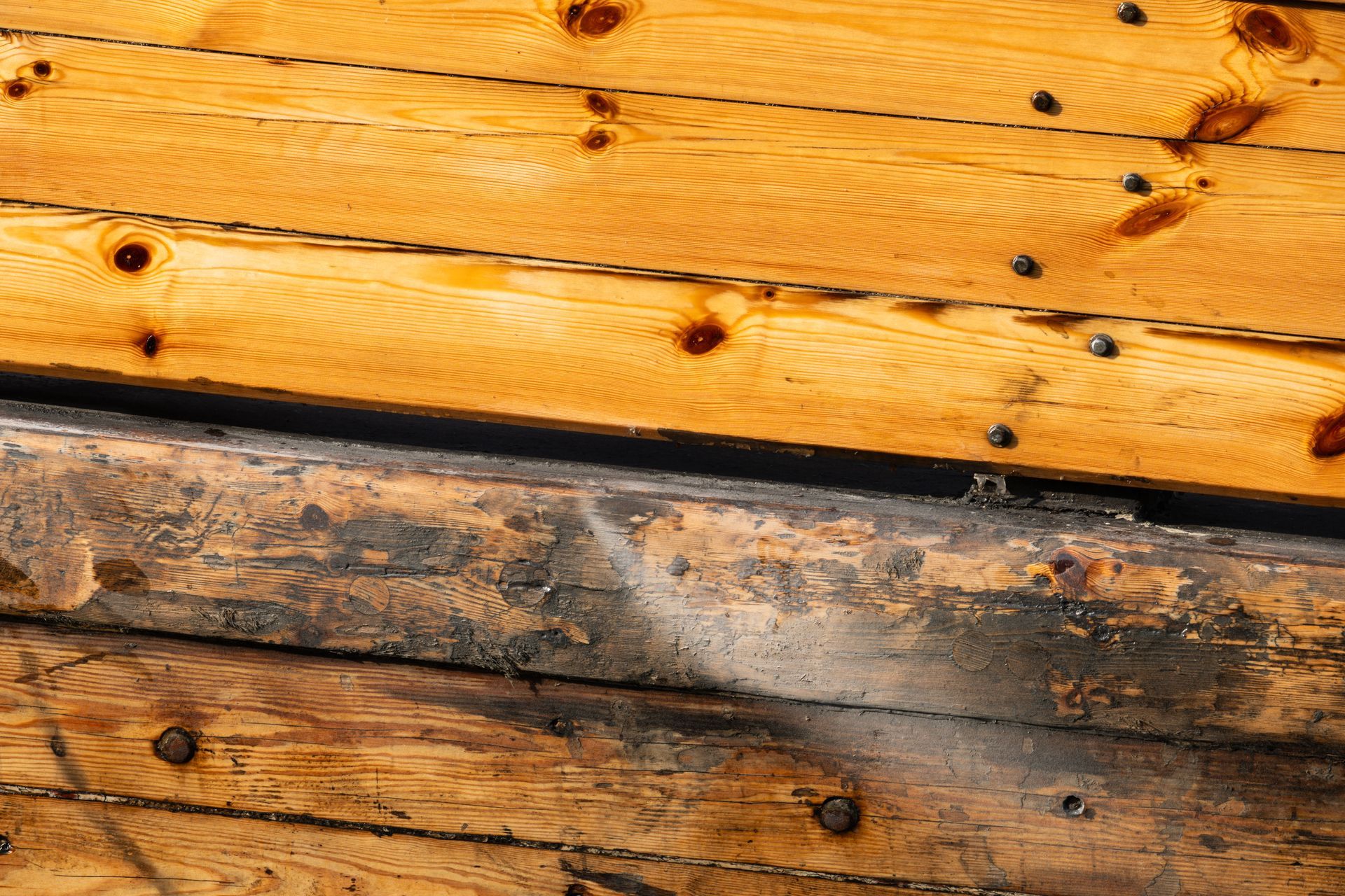 Close-up of wooden boat hull, showing light and dark wood planks, nails, and some discoloration.