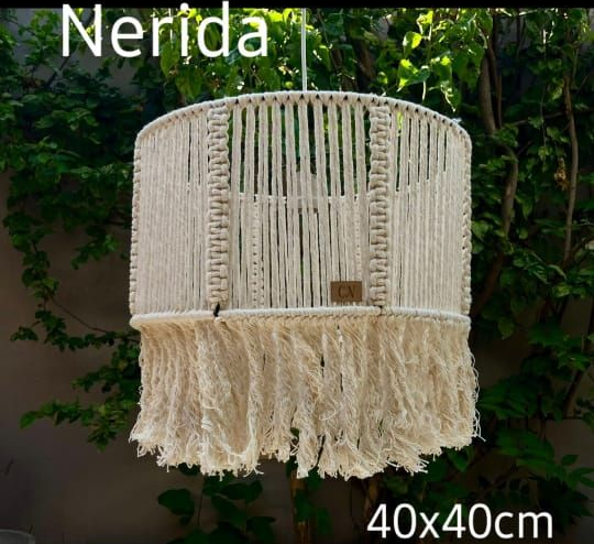 Pantalla de lámpara colgante de macramé color crema con flecos, 40x40 cm, sobre un fondo verde frondoso.