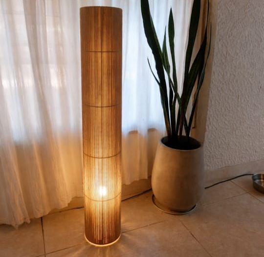 Lámpara de pie alta de bambú que brilla junto a una planta de serpiente en maceta en una habitación acogedora.