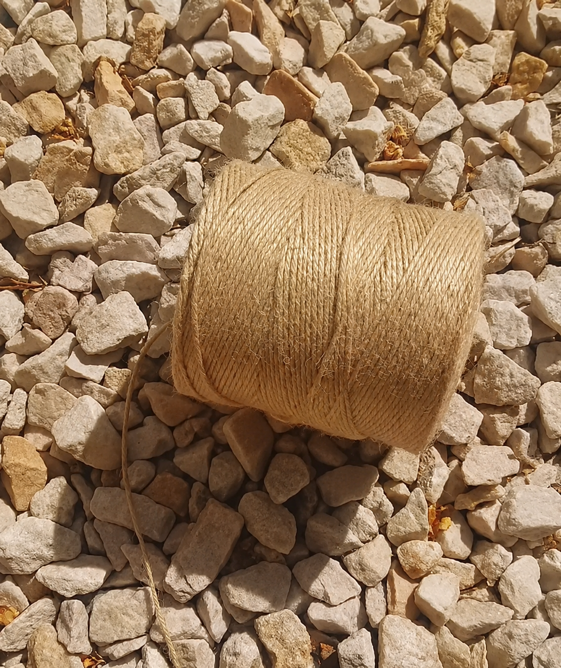 Carrete de hilo beige sobre piedras de grava clara bajo la luz del sol.