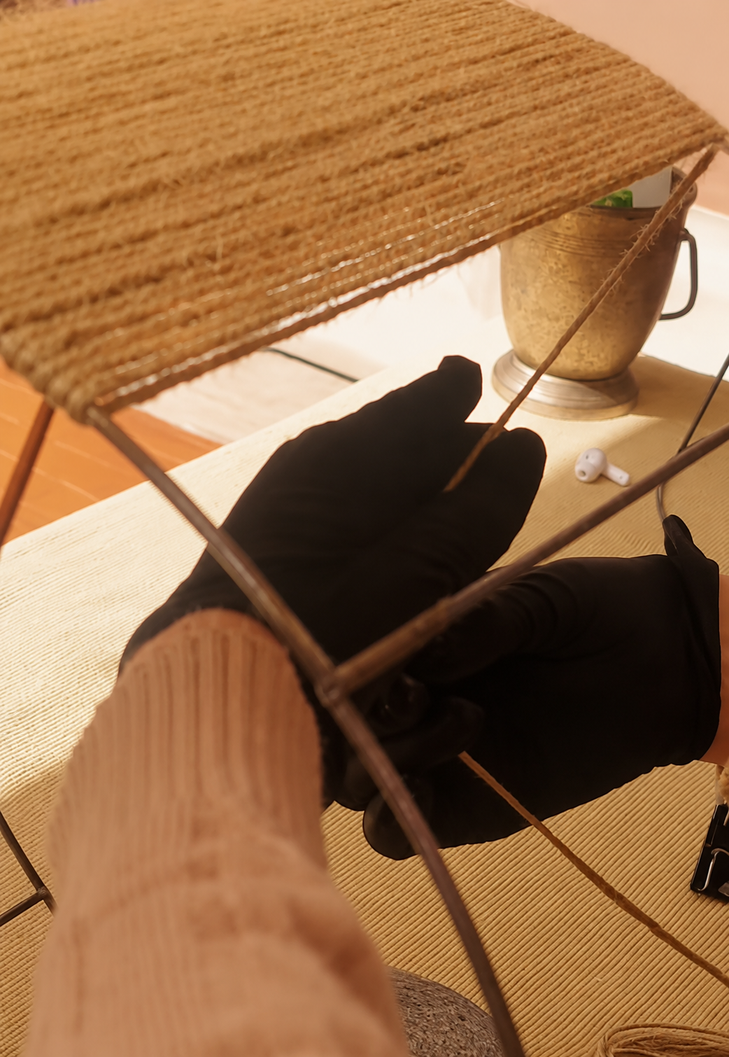 Un gato negro descansa bajo una mesa de mimbre, con la manga de un suéter beige en primer plano.