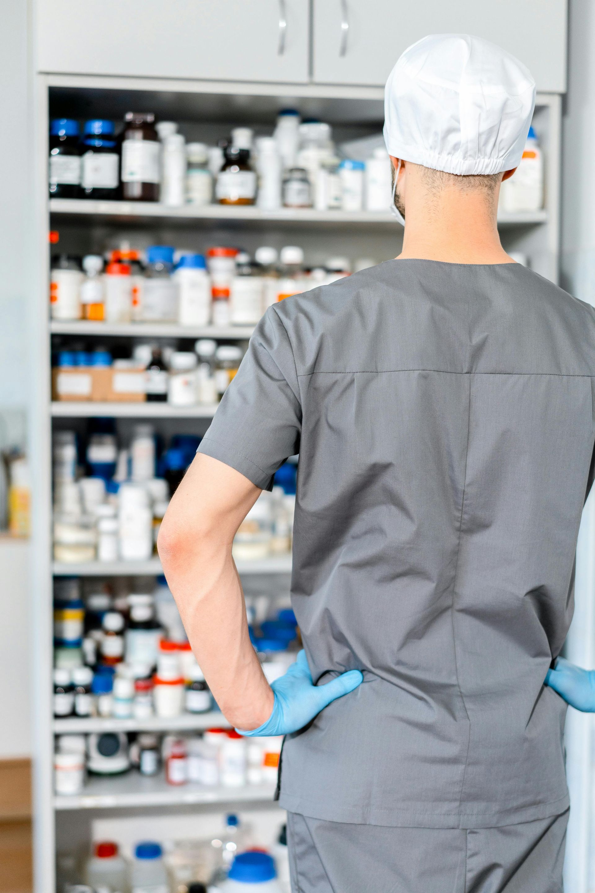 A female pharmacist is standing in front of a shelf in a pharmacy holding a clipboard.