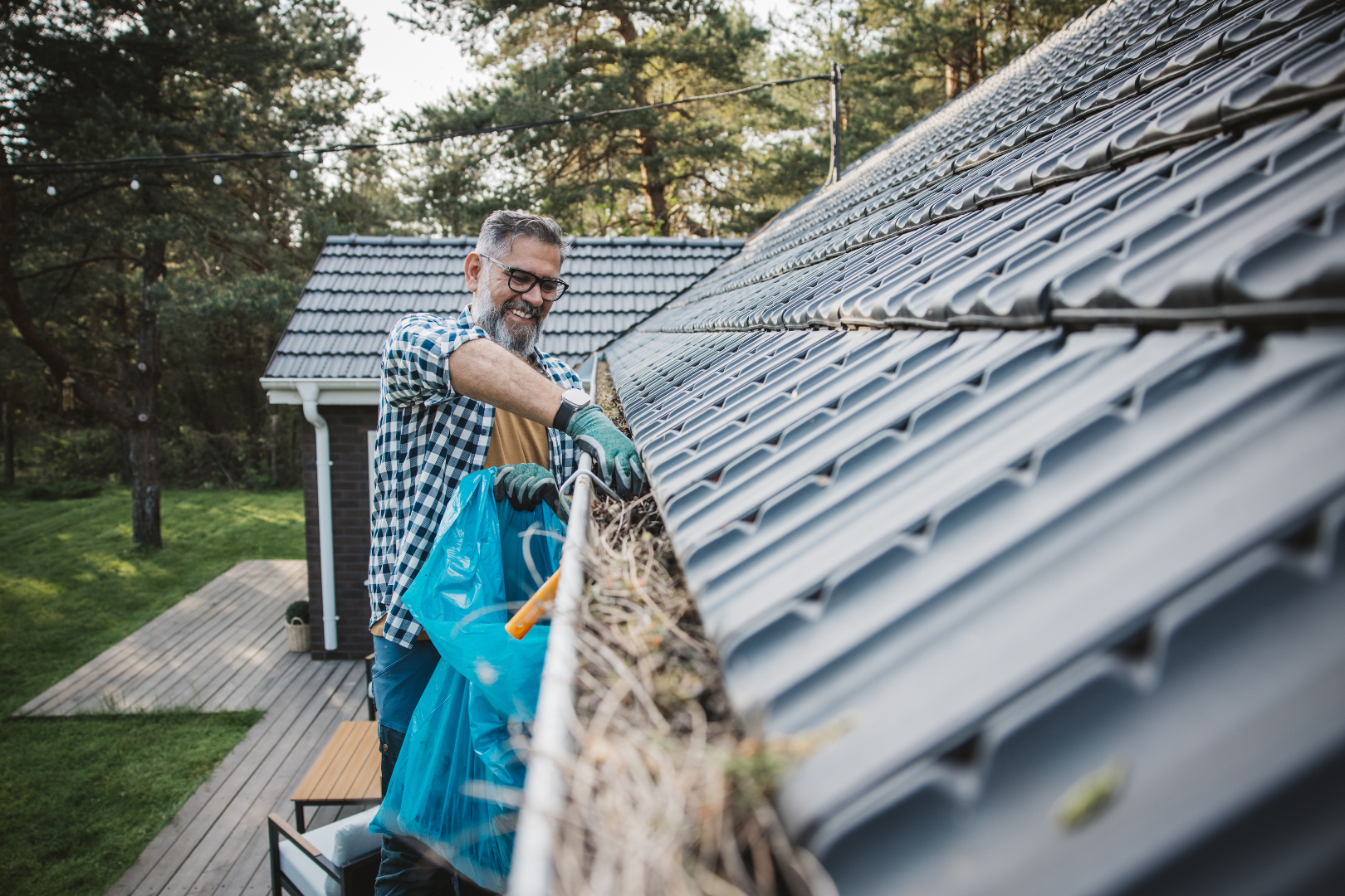 A man is cleaning a gutter on the roof of a house.