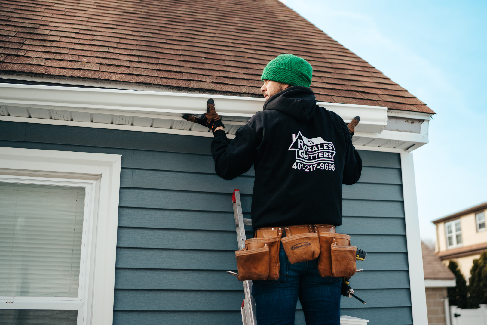 A man is fixing a gutter on the side of a house.