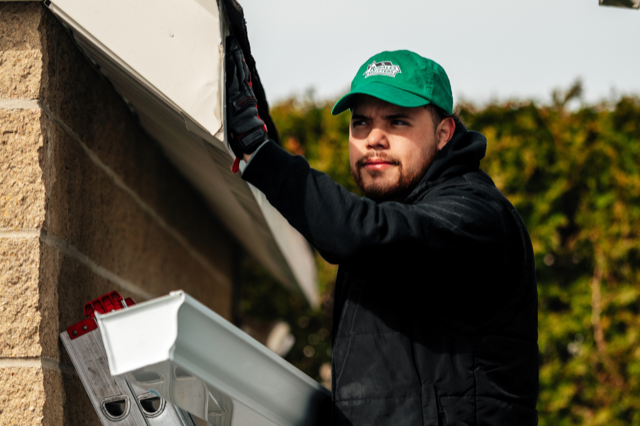 A man wearing a green hat is working on a gutter.