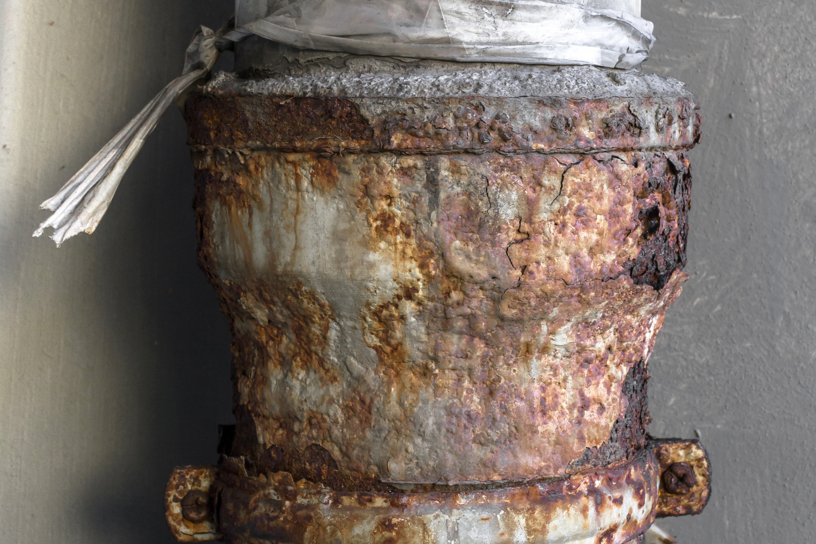 A close up of a rusty pipe with a white rope tied around it.