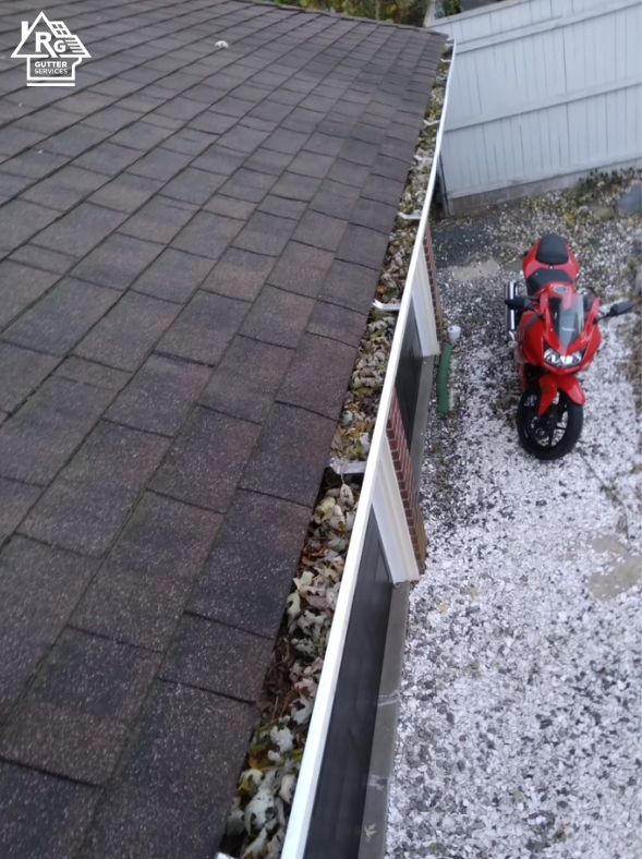 A red motorcycle is parked next to a gutter on a roof