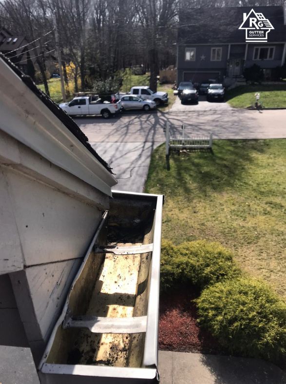 A gutter on the side of a house with cars parked in the driveway.