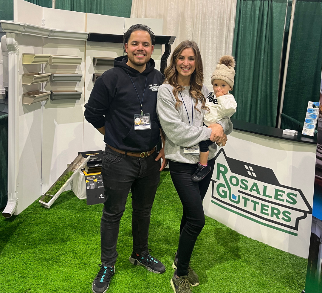 A man , woman and child are standing in front of a sign that says rosales gutters.