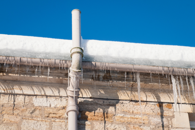 Icicles are hanging from a pipe on the side of a building.