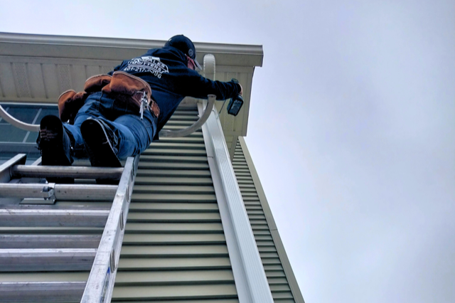 A man is climbing up a ladder on the side of a building.