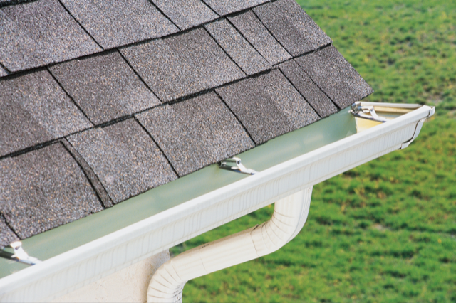 A close up of a gutter with a roof in the background