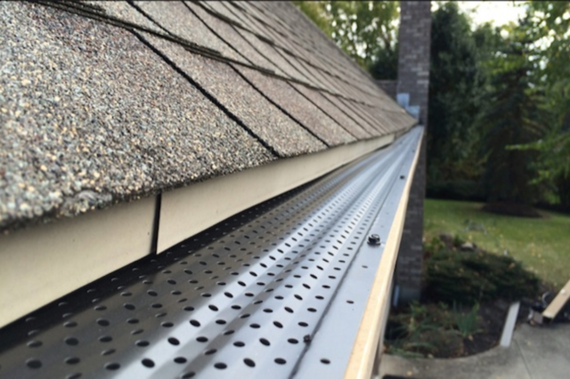 A gutter with holes in it is attached to a roof