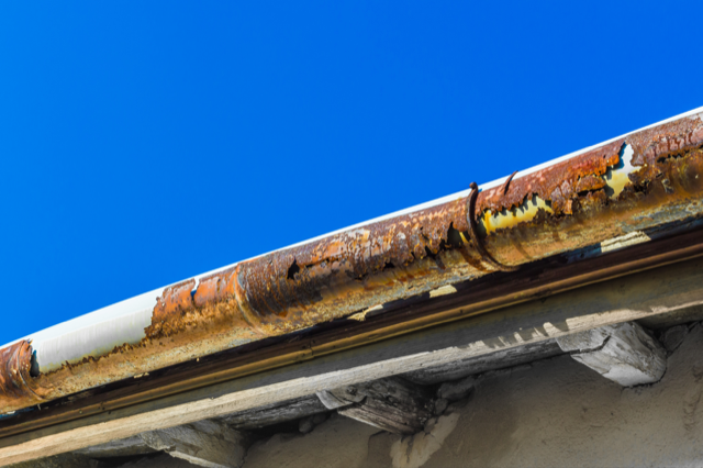 A rusty gutter on a roof with a blue sky in the background.