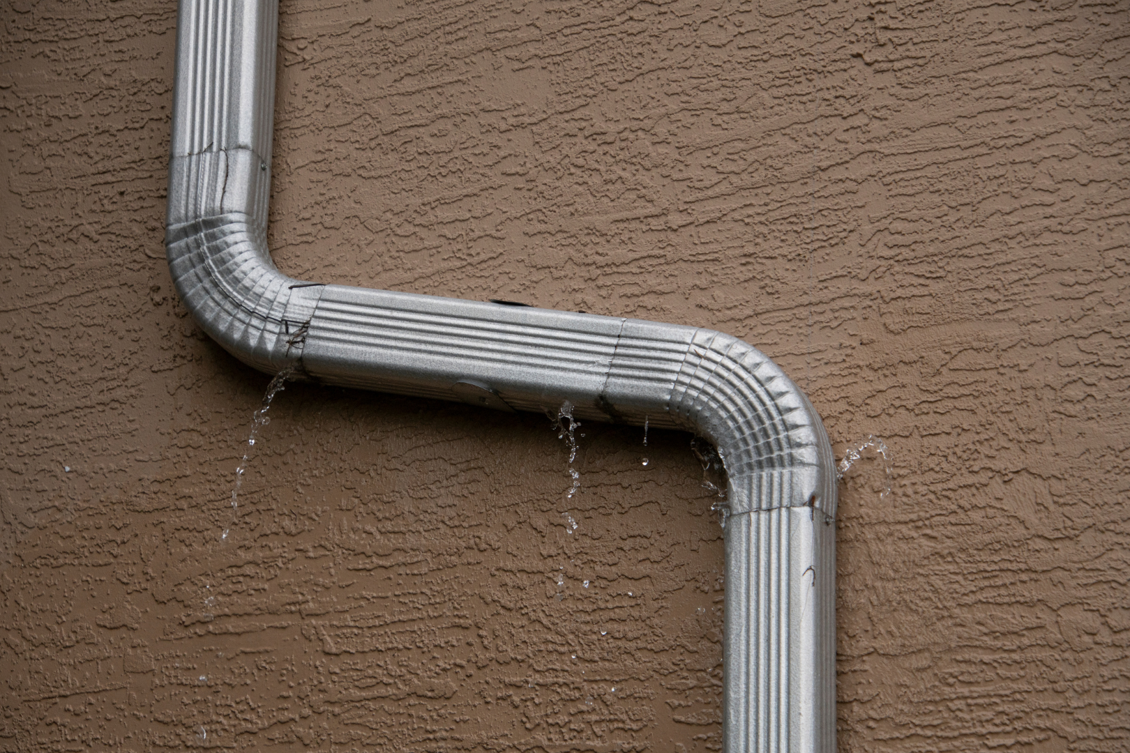 A gutter is leaking water on a brown wall.