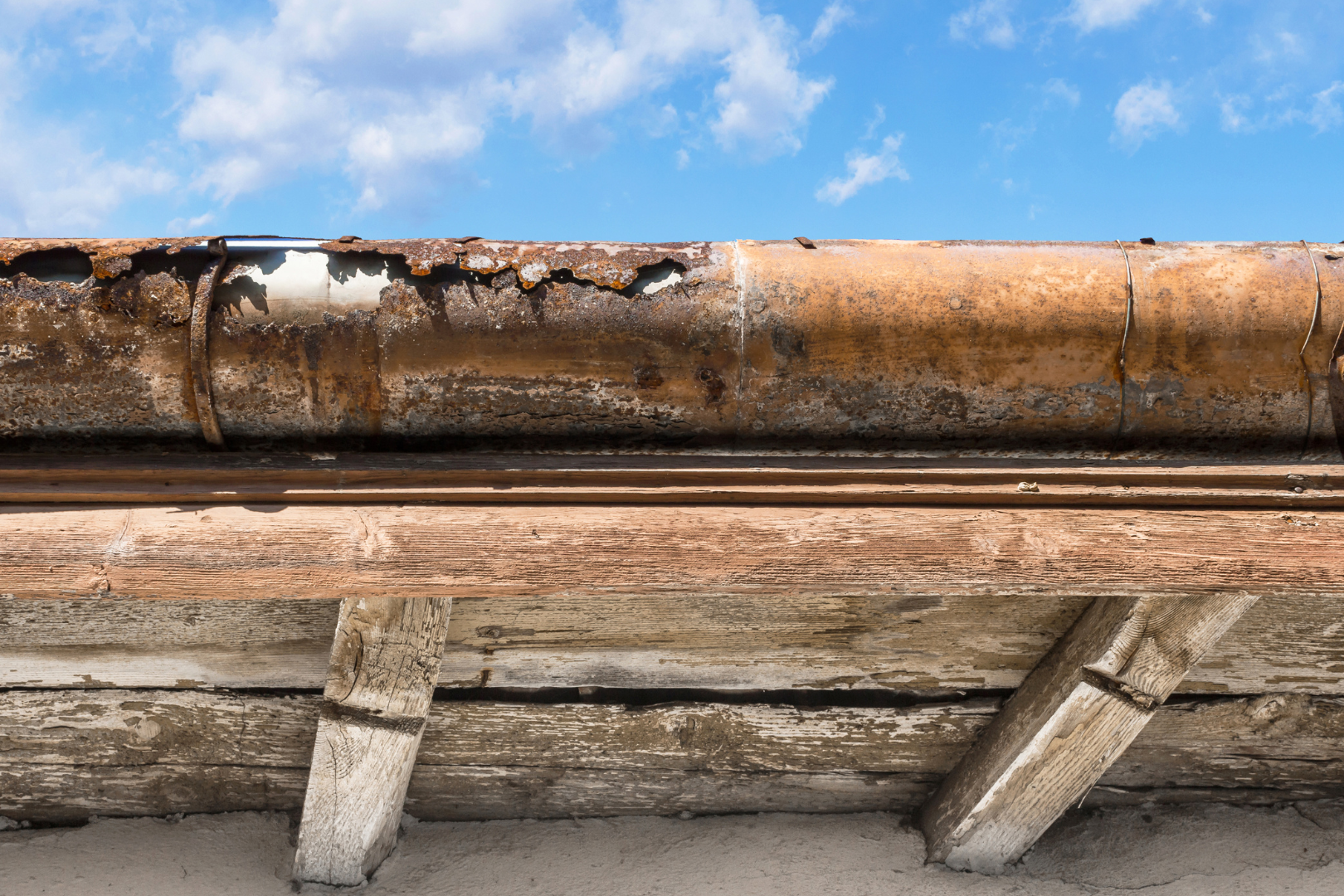 A rusty gutter on a roof with a blue sky in the background.