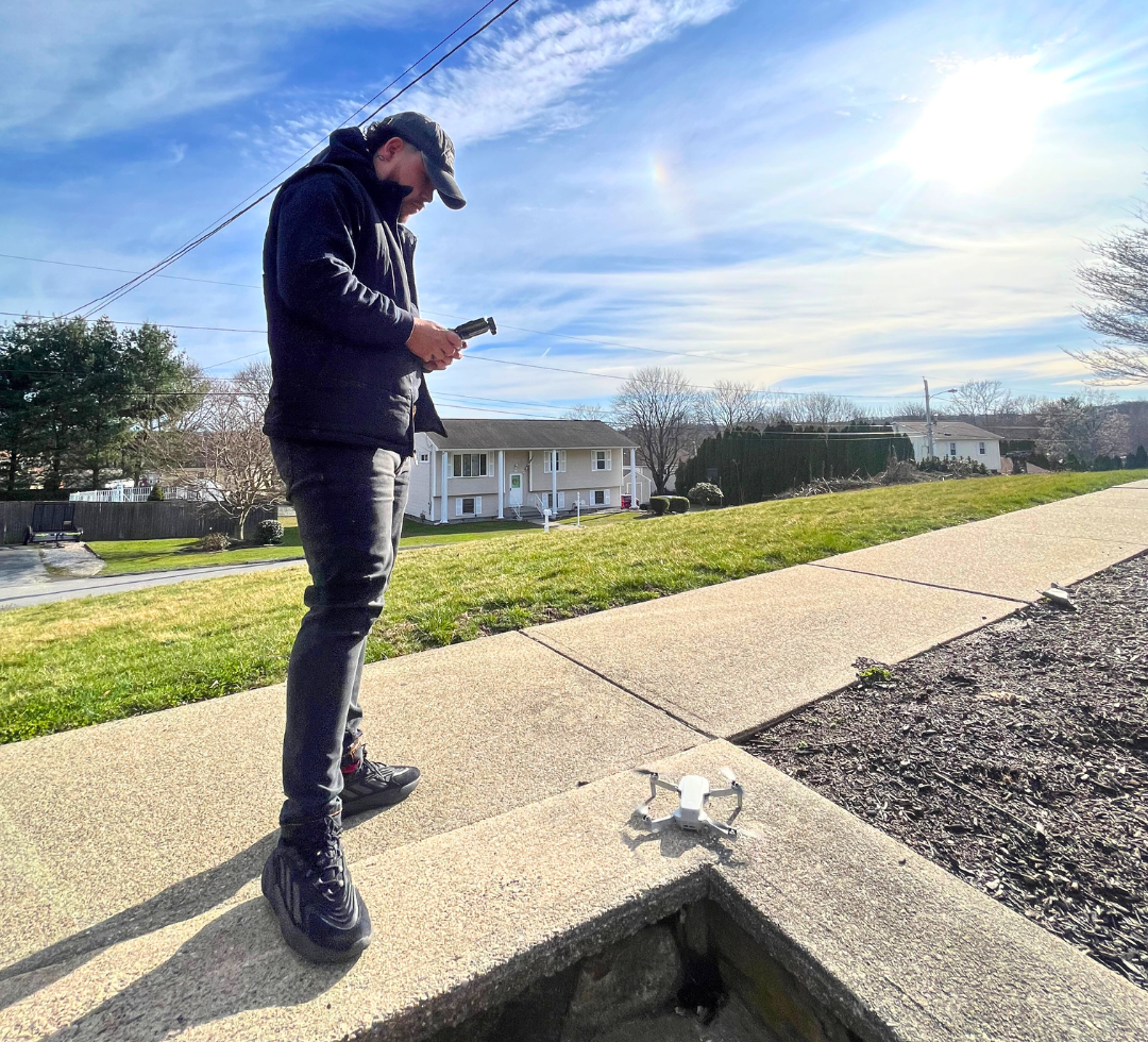 A man is standing on a sidewalk next to a drone.