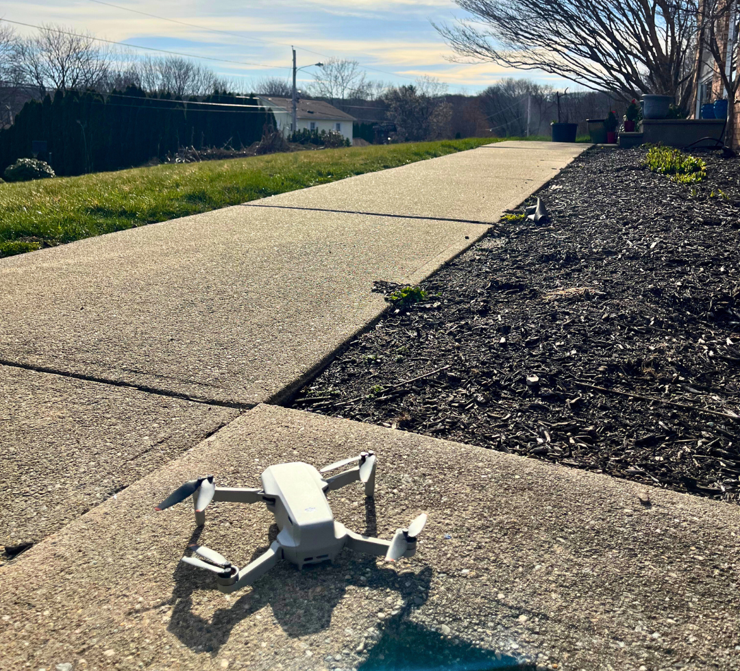 A drone is sitting on the sidewalk next to a sidewalk.