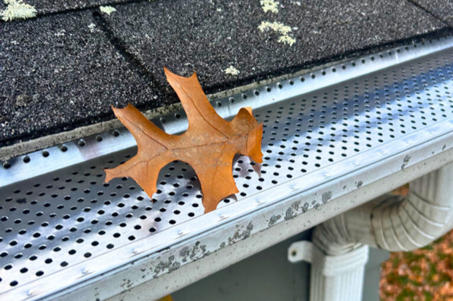 A leaf is sitting on top of a gutter on a roof.