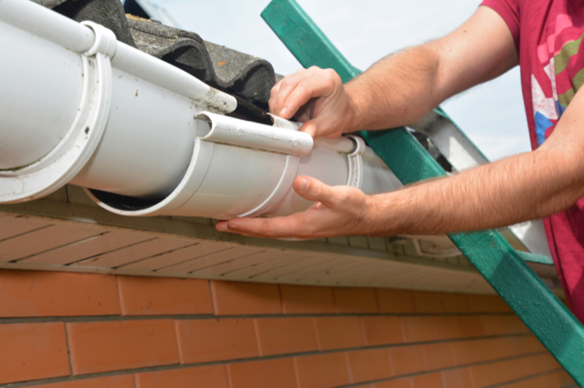 A man is installing a gutter on the roof of a house.