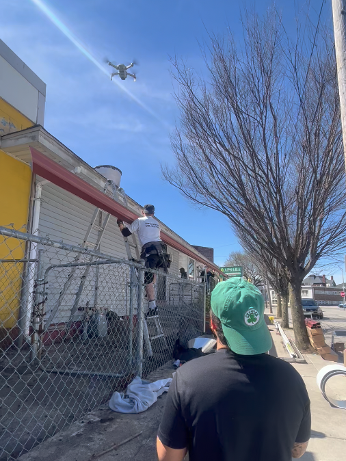 A man in a green hat is looking at a drone flying over a building