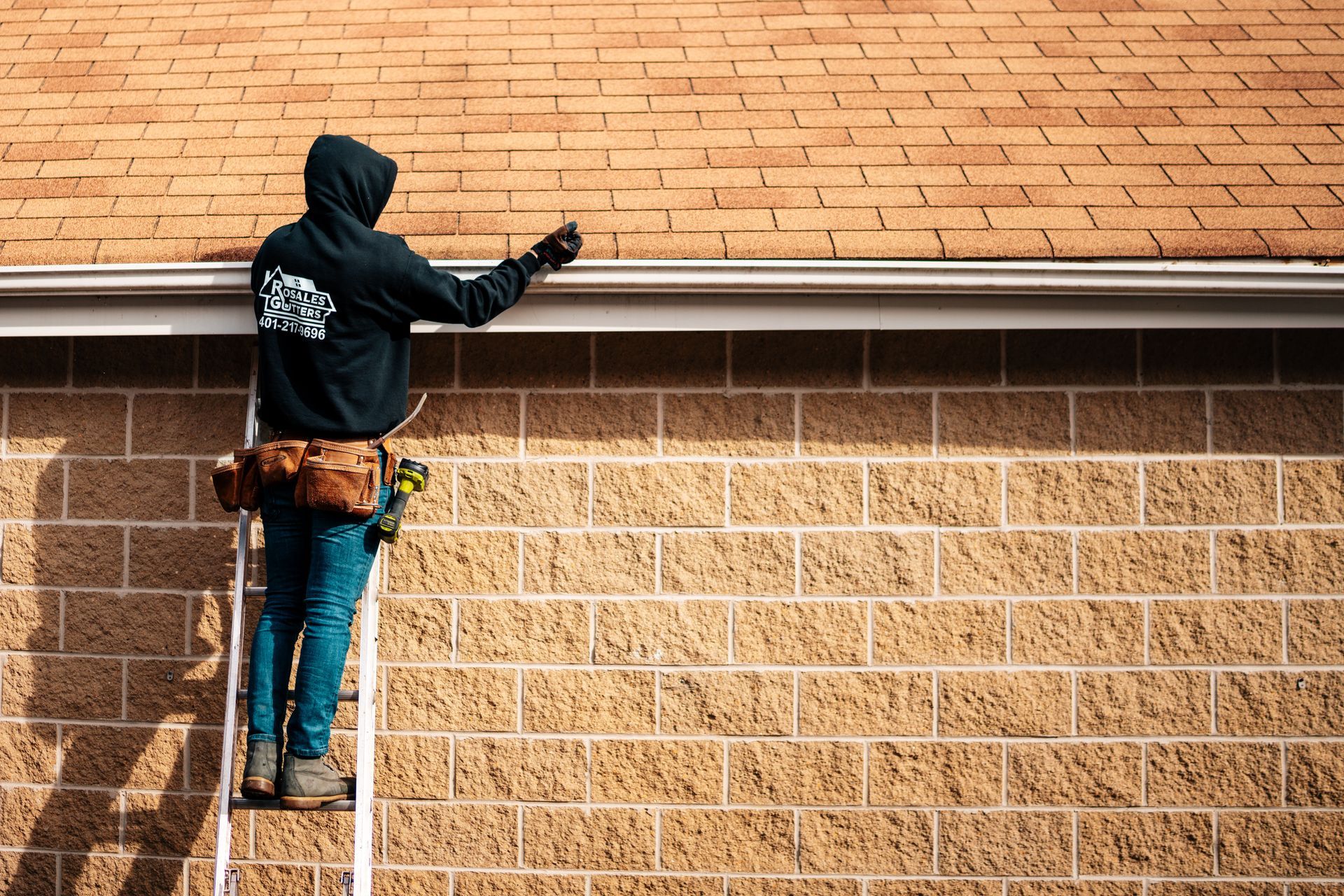 A man is standing on a ladder on the side of a brick building.