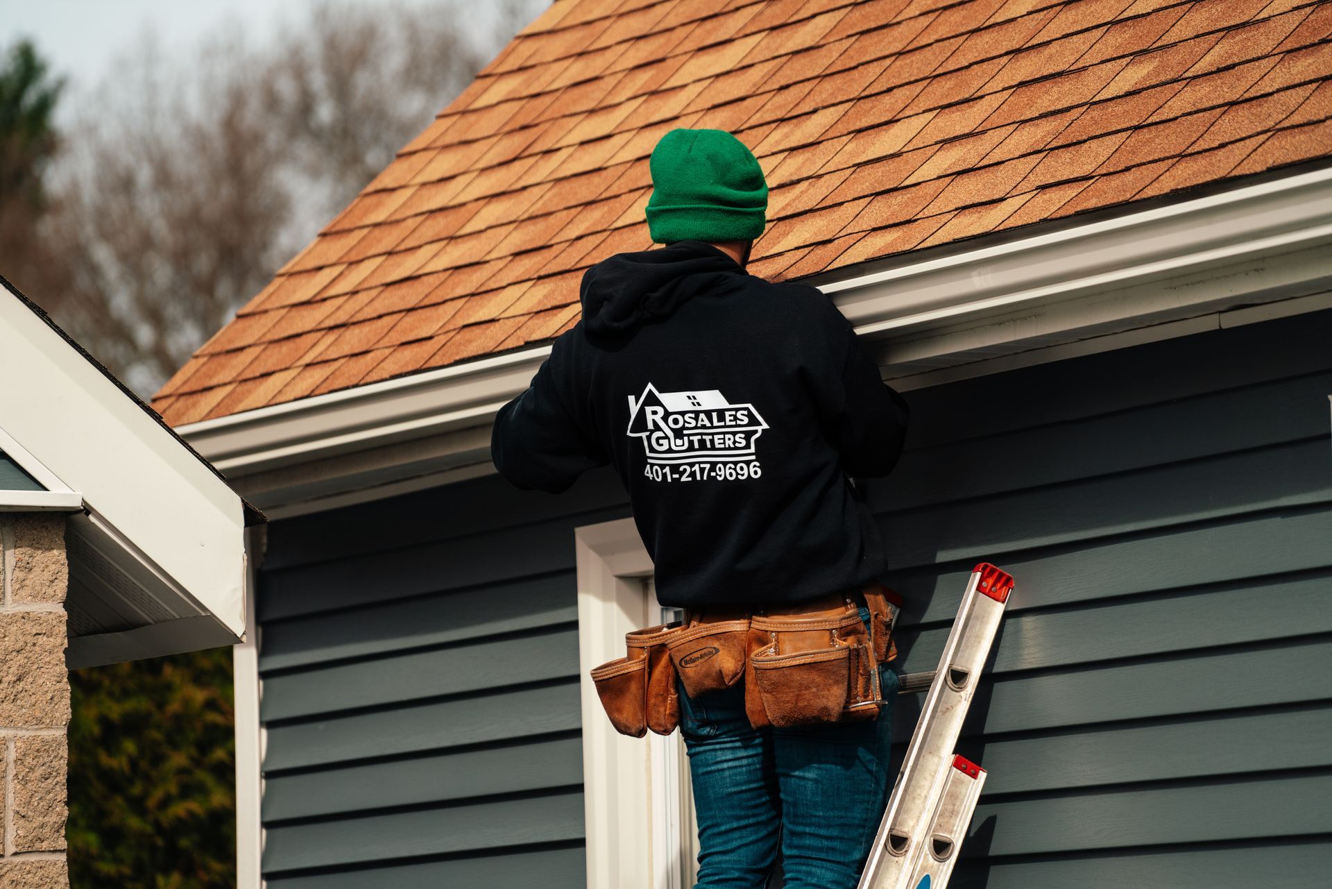 A man is standing on a ladder on the side of a house.