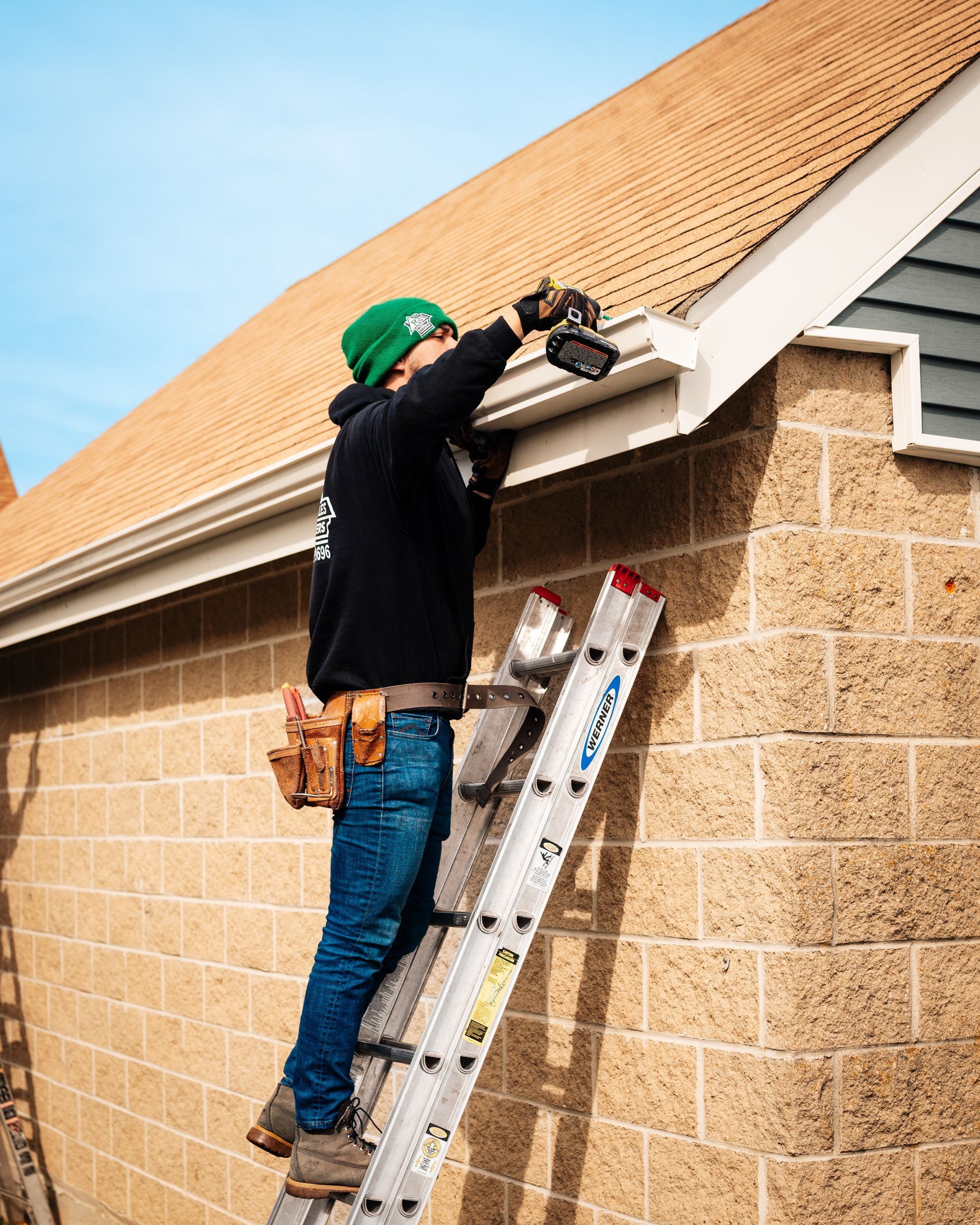 A man is standing on a ladder working on the roof of a house.