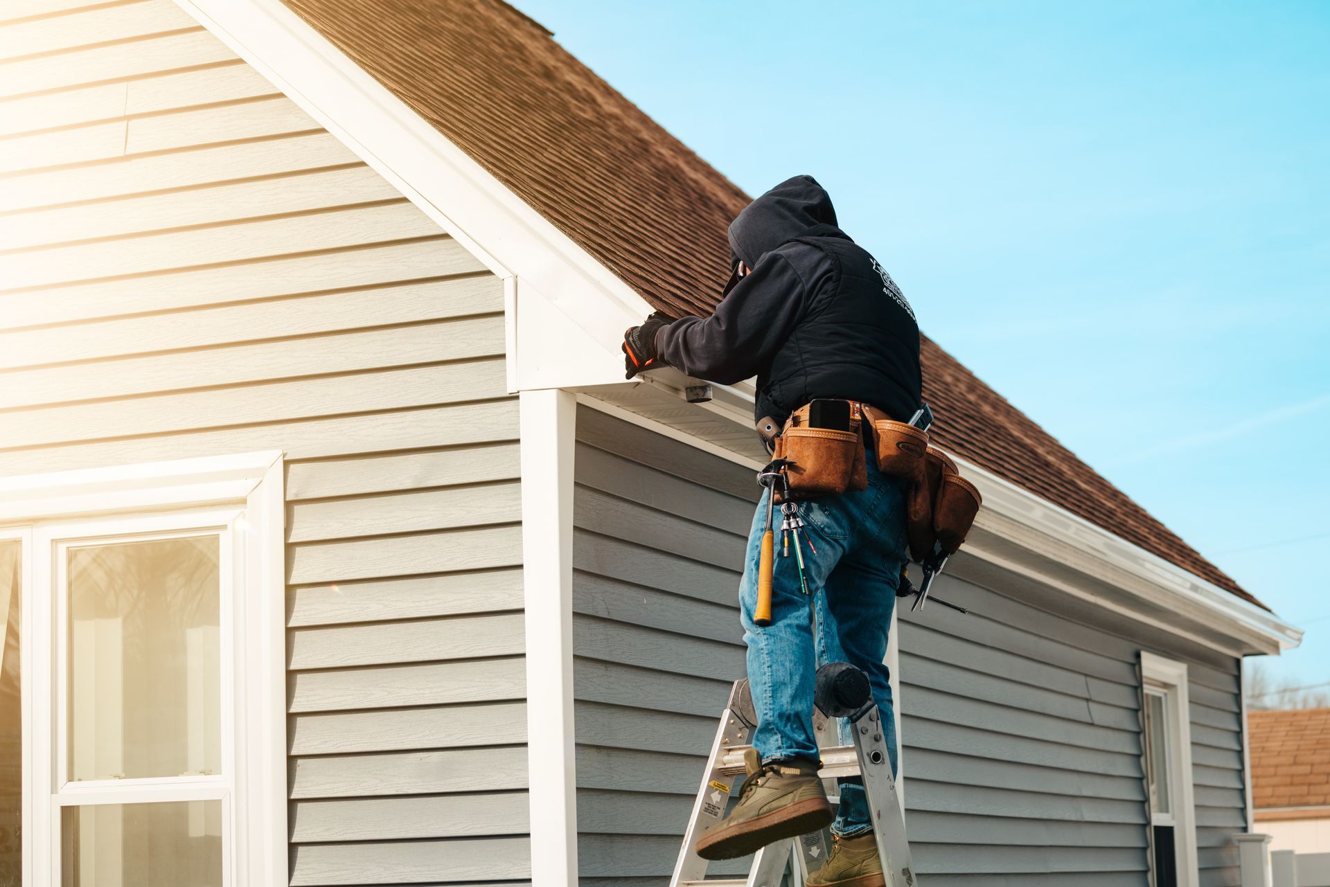 A man is standing on a ladder working on the roof of a house.