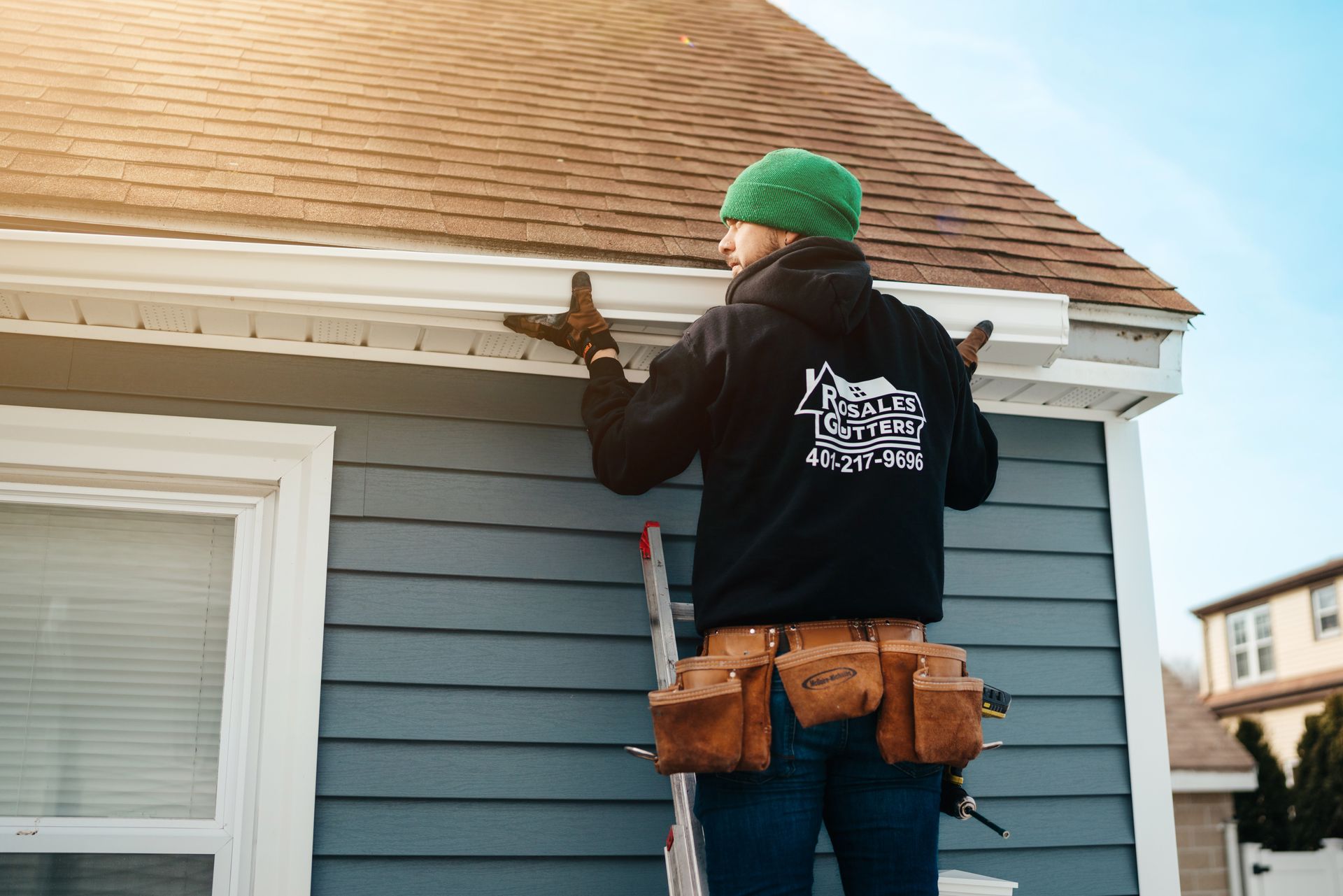 A man is installing a gutter on the side of a house.