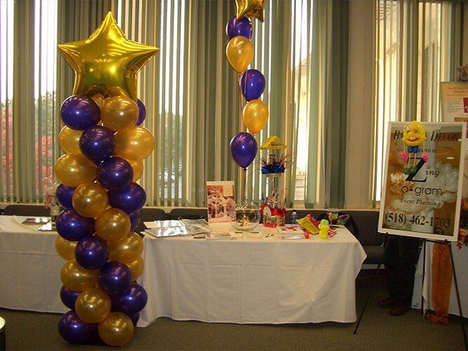 Purple and gold balloon columns beside a decorated table at an indoor party display