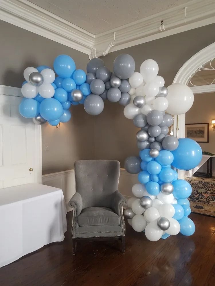 Blue, white, and gray balloon arch around a gray armchair in a decorated room