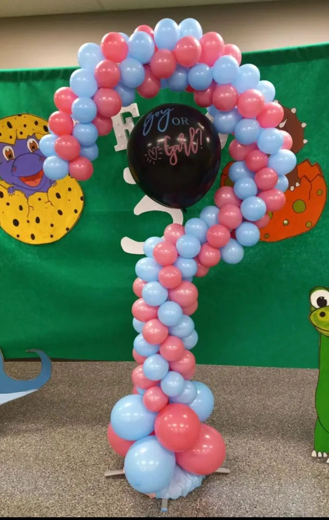 Pink and blue balloon arch shaped like a question mark on a decorated party backdrop