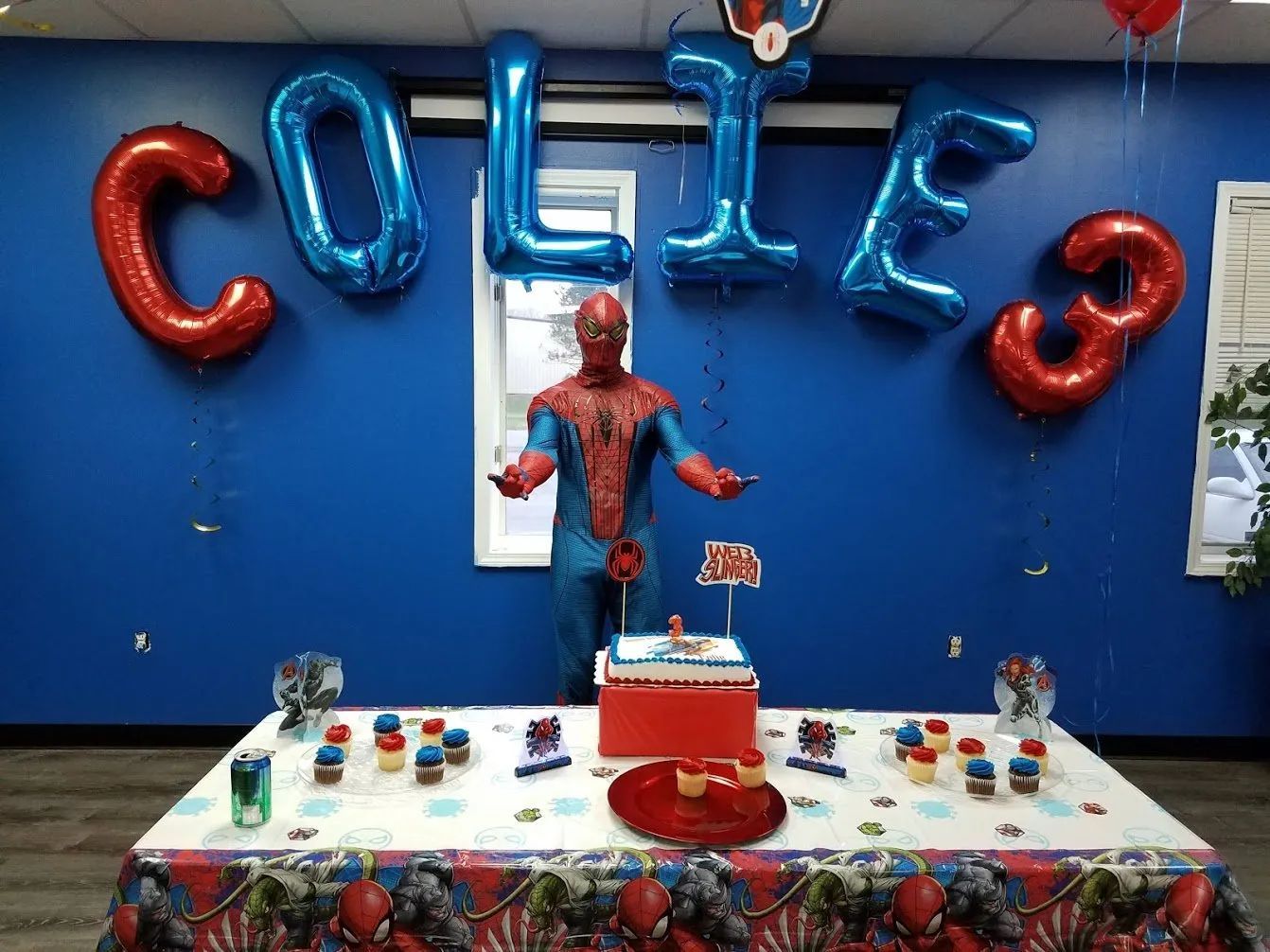Spider-Man birthday table with red and blue decorations and COLIE balloon letters on a blue wall