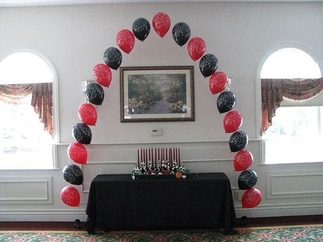 Red and black balloon arch over a black table in a room with arched windows and a framed wall picture.