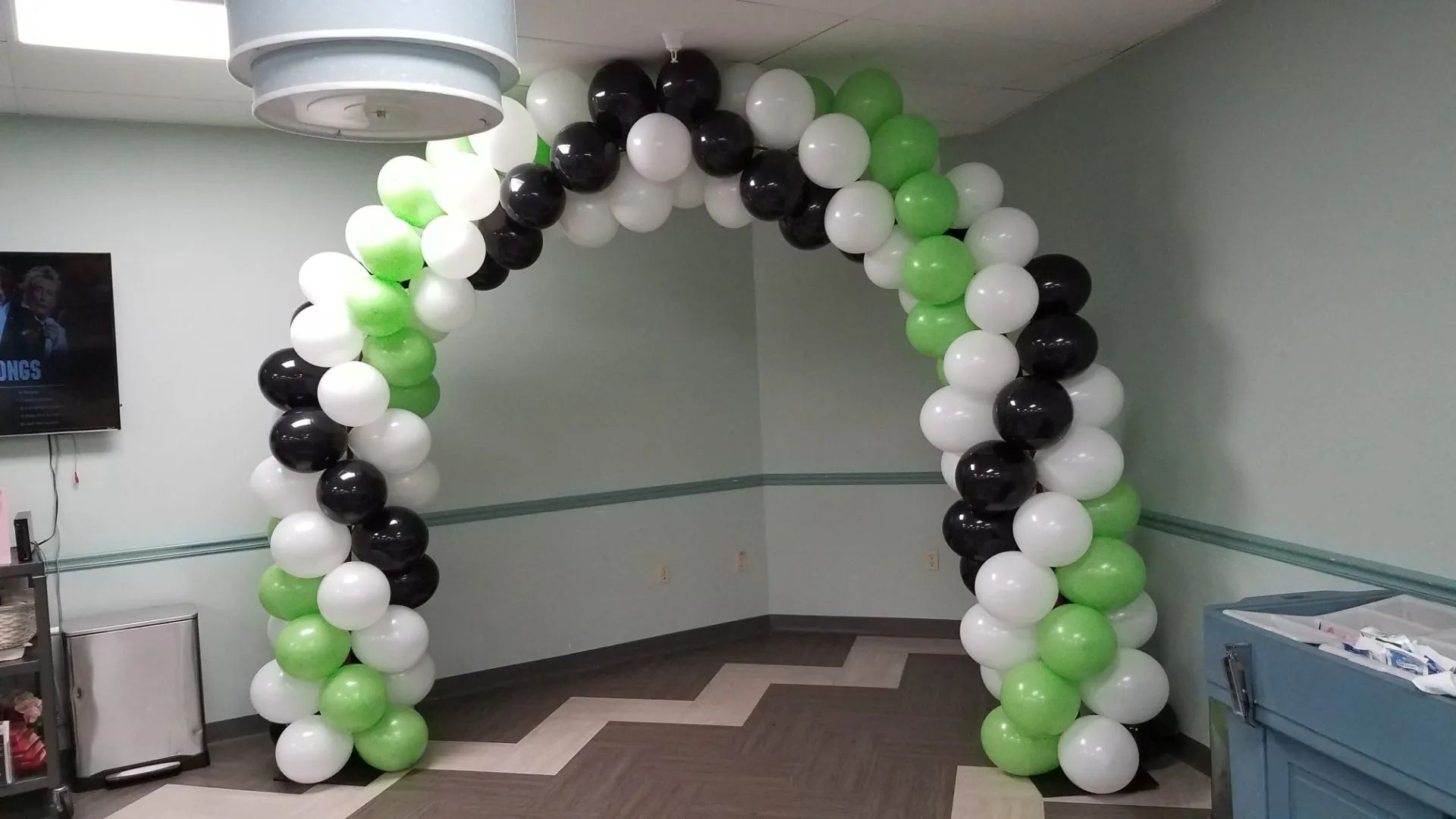 Black, white, and green balloon arch in a room corner for an event display.
