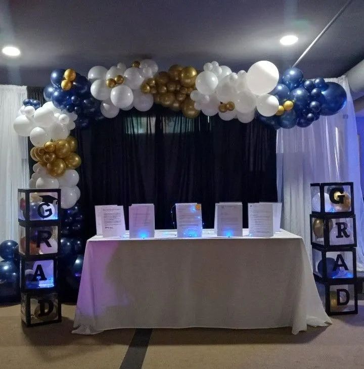 Graduation party display with balloon arch, dessert table, and glowing “GRAD” light boxes