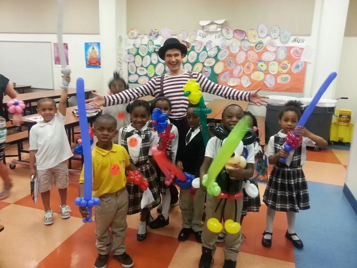 Children posing with colorful toy swords in a classroom, with a smiling teacher in the center.