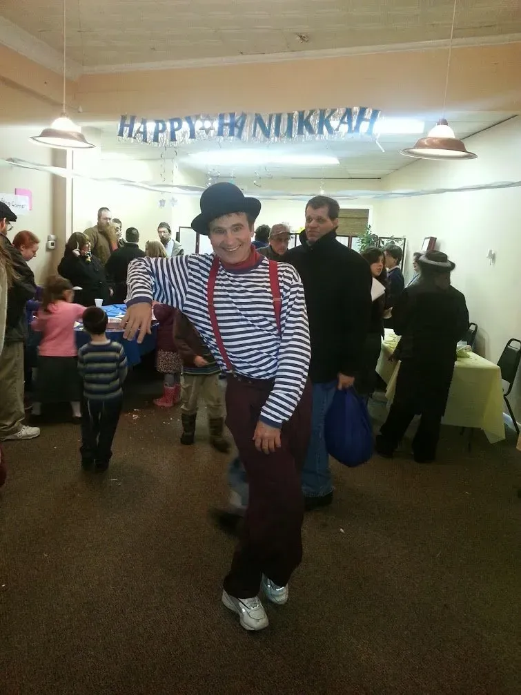 Person in a striped shirt, red suspenders, and top hat dancing at a festive indoor party.
