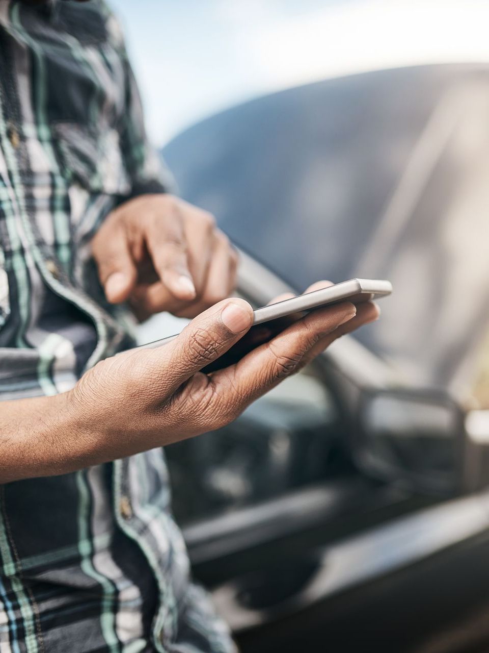 A man is using a cell phone in front of a car.