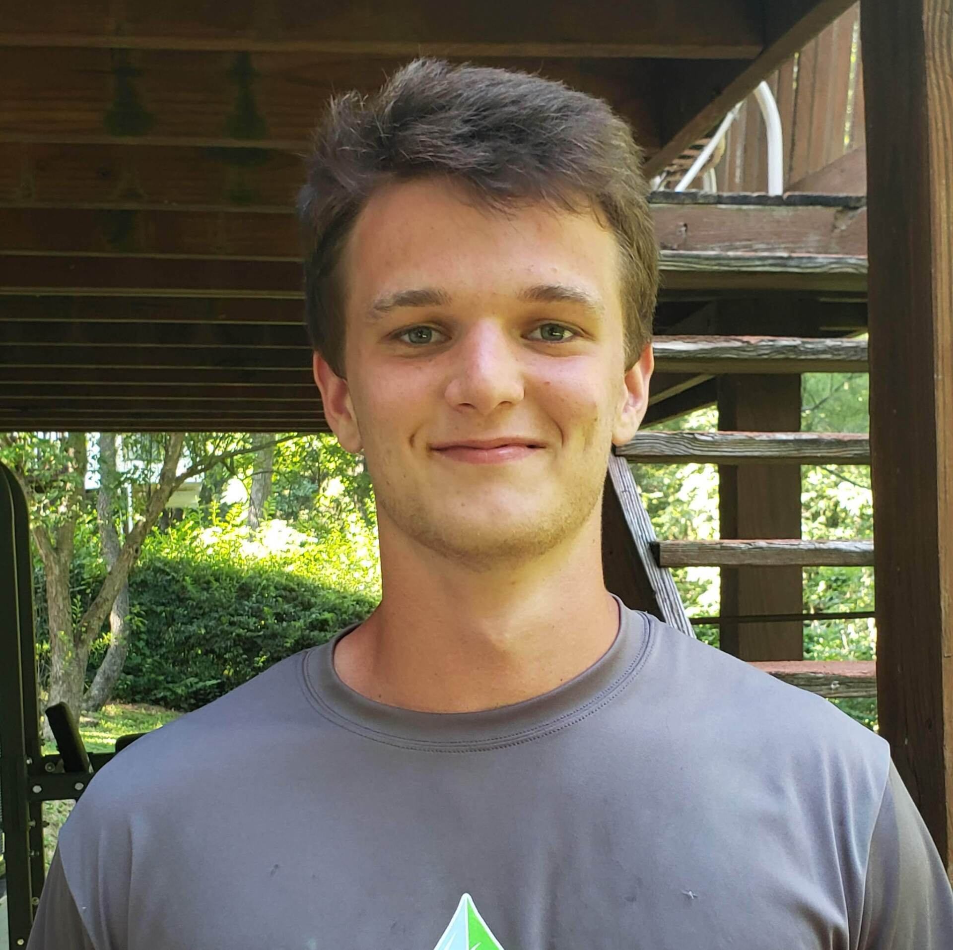 A young man wearing a gray shirt is standing in front of stairs.