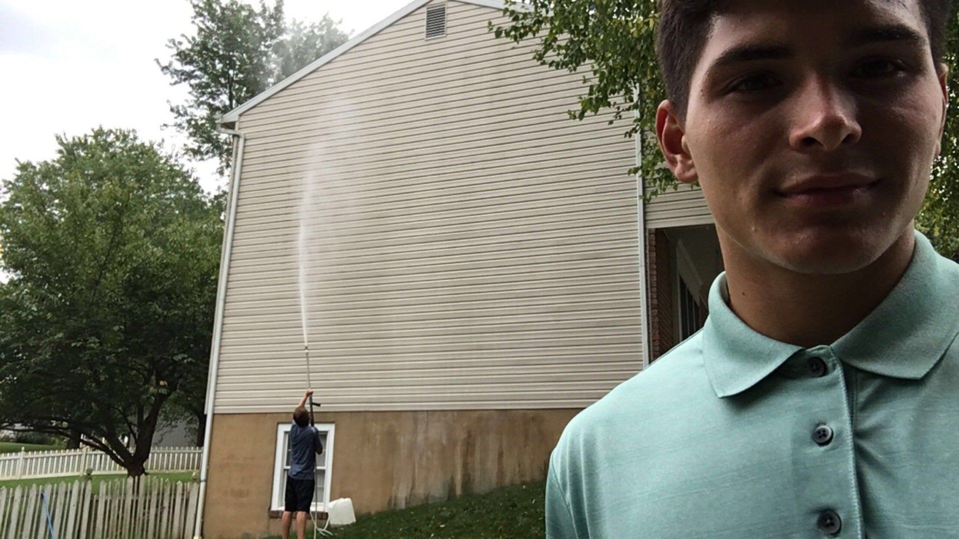 A man in a green shirt is standing in front of a house.