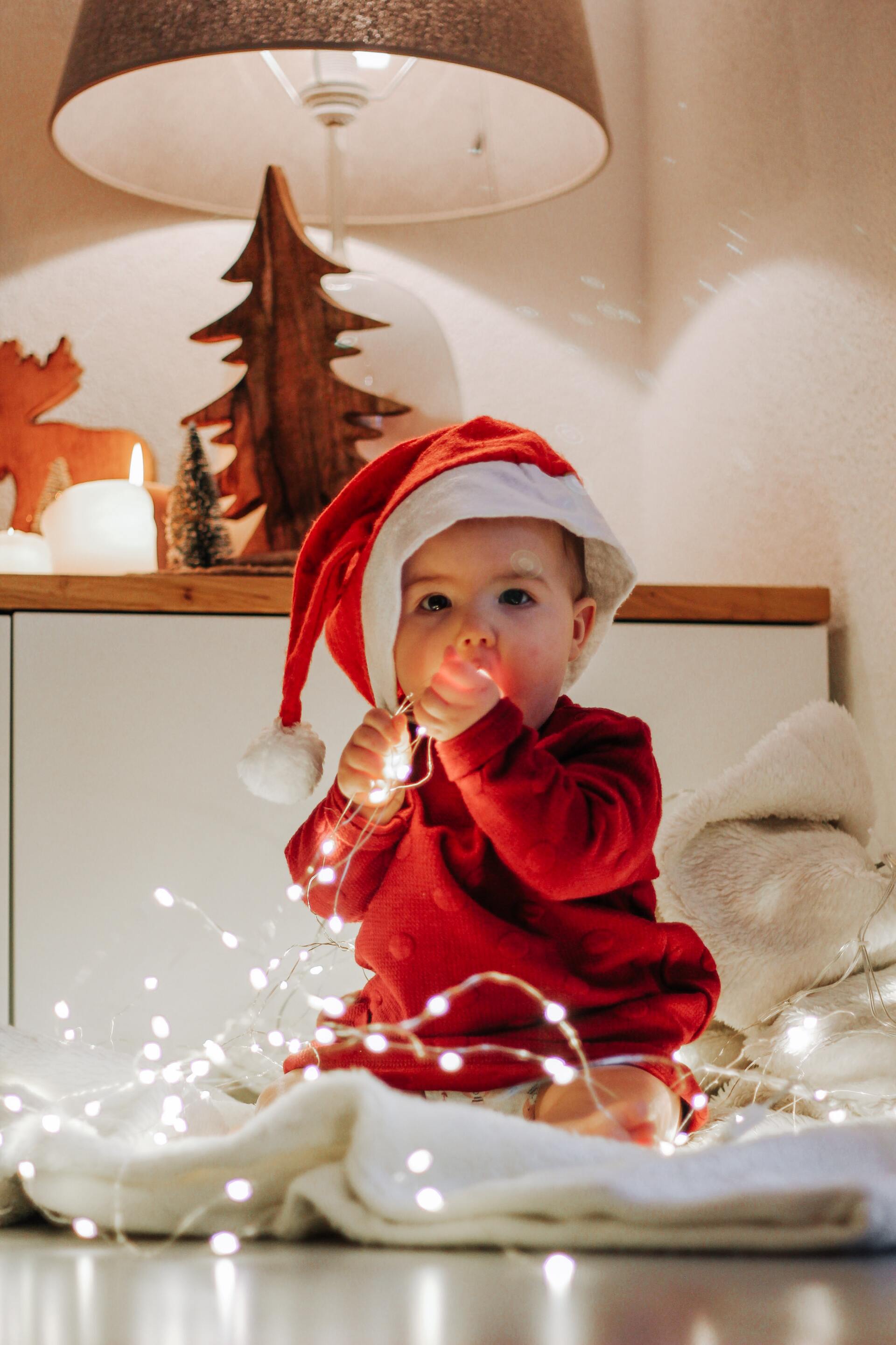 A baby is wearing a santa hat and playing with christmas lights.