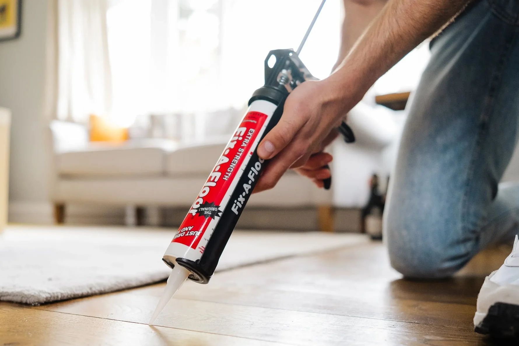 Person wearing glove using a trowel to apply grout to tile seams on a gray tiled floor.