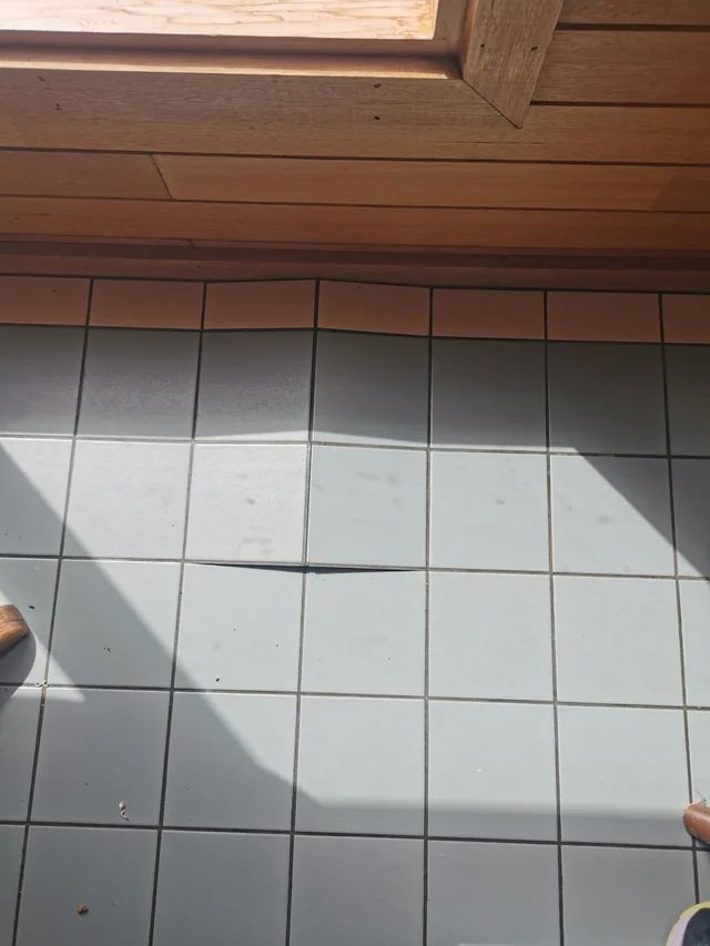 Hand scrubbing a diamond-shaped gray tile with green scrub brush; soapy water present.