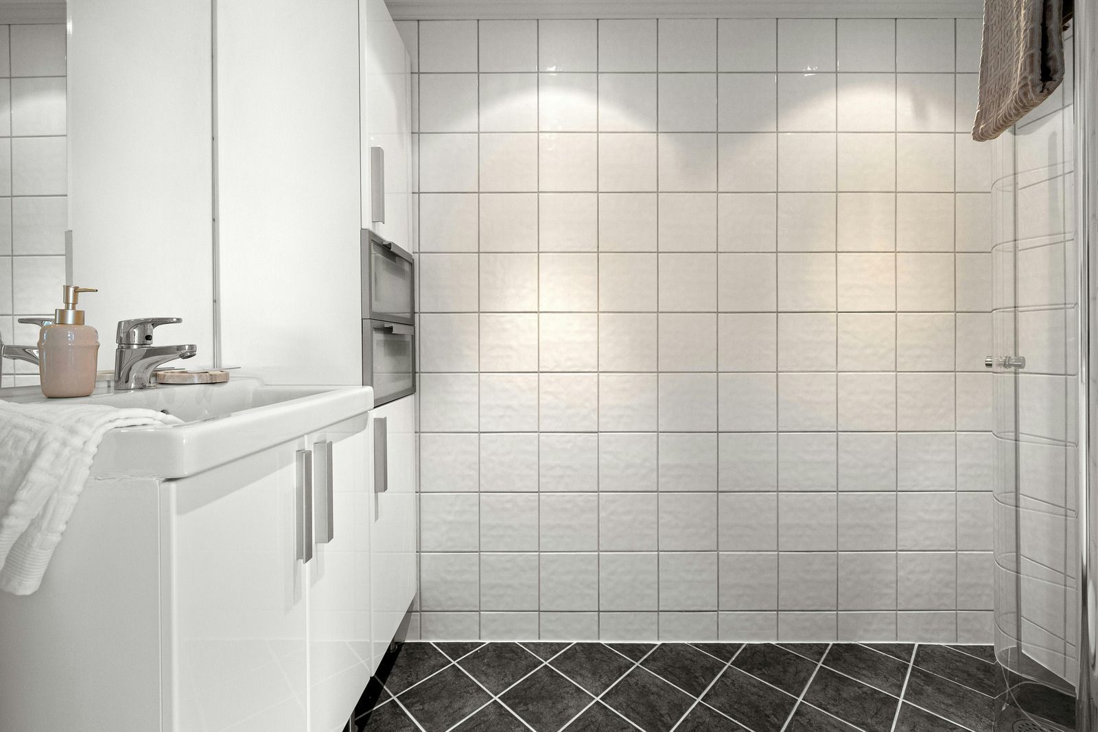 White bathroom with sink, cabinet, tiled walls, dark floor, and glass shower.