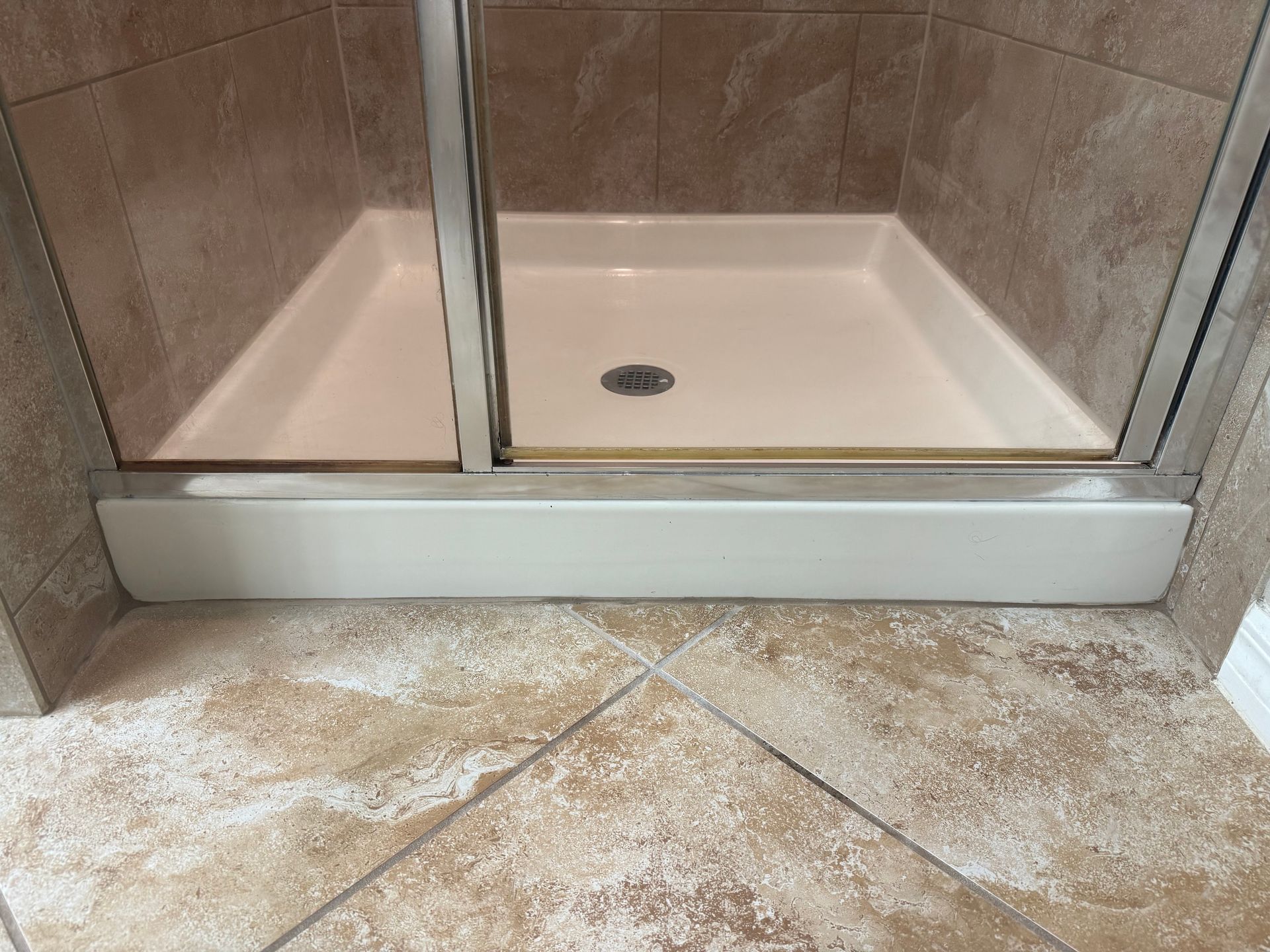 Shower stall with white base, glass doors, and tan tile walls and floor.