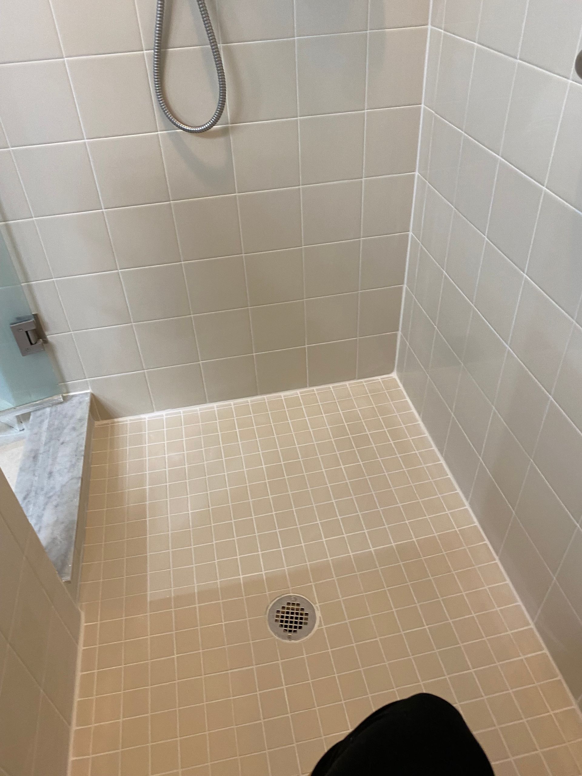Shower stall with beige tiles, showerhead, and drain.