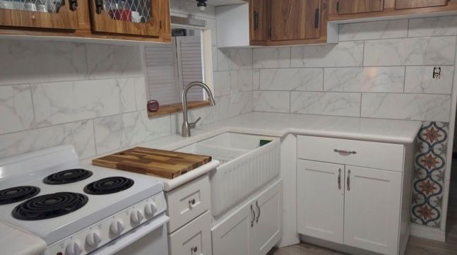 White kitchen with wooden cabinets, white countertops, stove, and farmhouse sink.